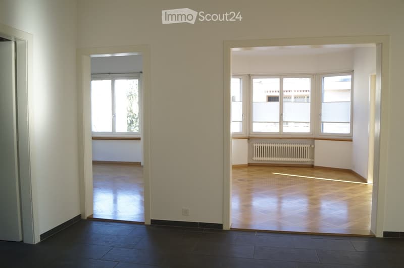 Empty hallway with two adjacent unfurnished rooms, featuring wooden flooring, large windows, and white walls.