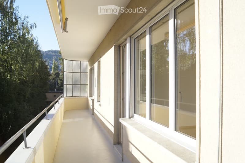 Balcony with white flooring, metal railing, large windows, and scenic view of greenery and hills.