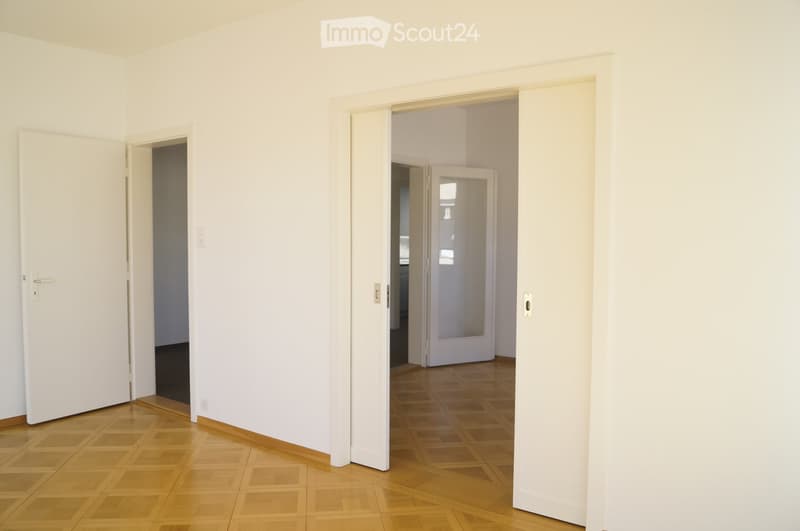 Empty room with light-colored walls and wooden flooring, featuring multiple open doors leading to adjacent spaces.