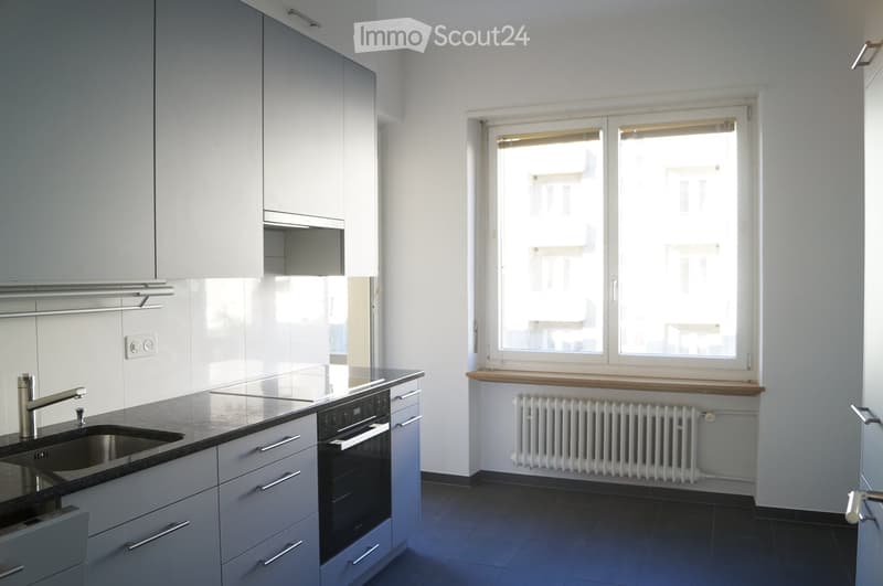 Modern kitchen with white cabinets, stainless steel sink, oven, and a window with radiator below.