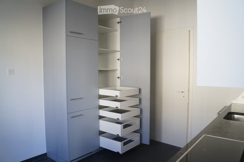 Modern kitchen with grey cabinet featuring multiple drawers and shelves, white countertop, and stainless steel sink.