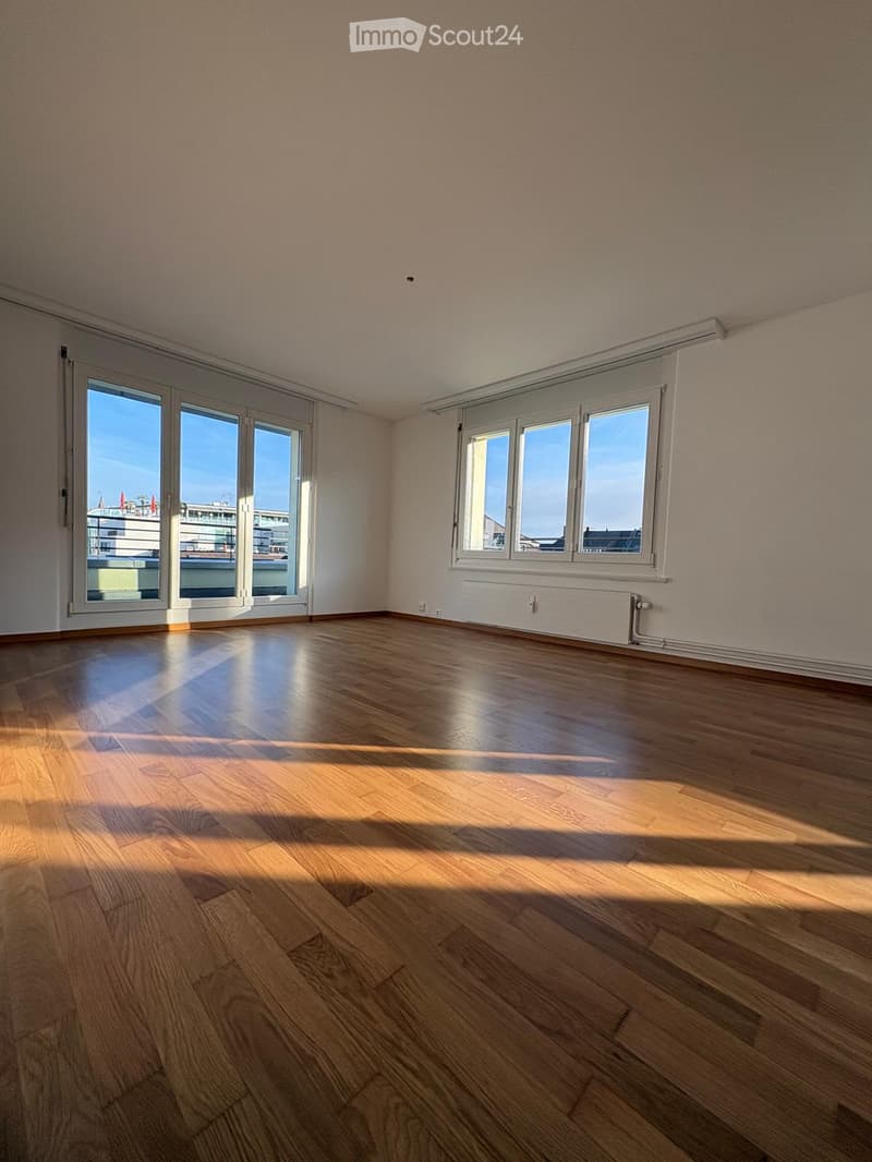 Empty room with wooden flooring, large windows, and sliding glass doors leading to a balcony.