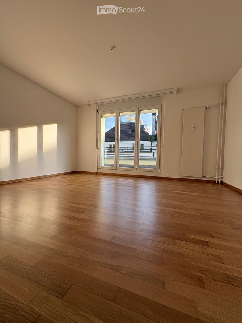 Empty room with wooden flooring, large sliding glass doors, and natural light from the left side.