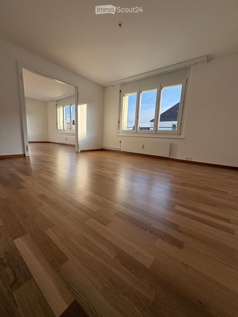 Empty room with wooden flooring, large windows, and white walls. No furniture or equipment present.