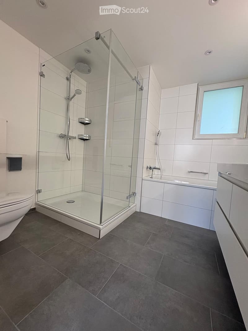Modern bathroom with a glass-enclosed shower, toilet, bathtub, and a window providing natural light.