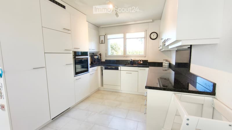 Modern kitchen with white cabinets, black countertops, and stainless steel appliances including a refrigerator, oven, and dishwasher. Features a large window, a sink with a faucet, and a coffee maker on the counter.