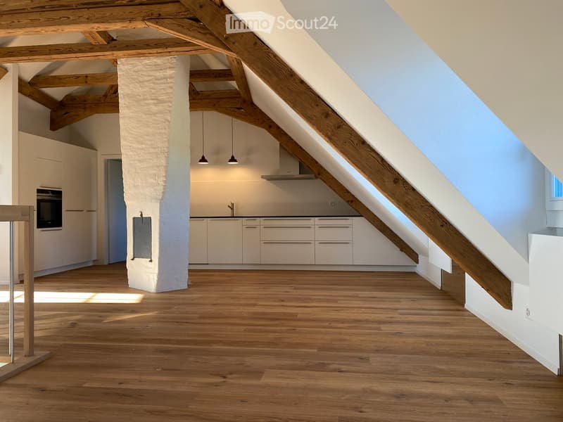 Open-plan attic space with wooden beams, light-colored cabinets, and a modern kitchen area.