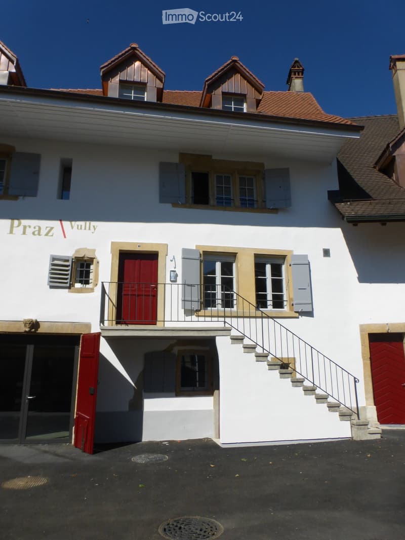 Two-story white building with red doors, multiple windows, and a small balcony accessed by stairs.
