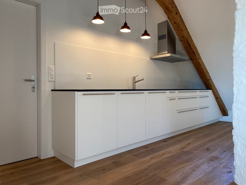 Modern kitchen with white cabinets, wooden flooring, and a stainless steel range hood. Features a sleek faucet and built-in lighting.