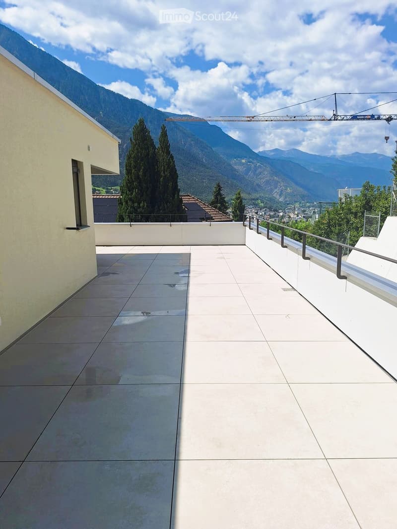 Modern rooftop terrace with clean lines, white tiles, and a metal railing, overlooking a scenic mountain landscape.