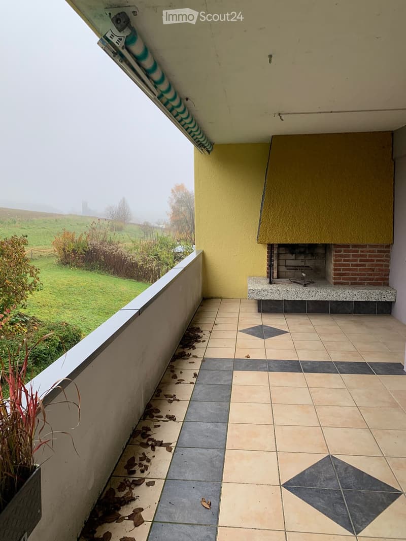 Balcony with tiled floor, yellow wall, small seating area with a brick fireplace, and a view of a green landscape.