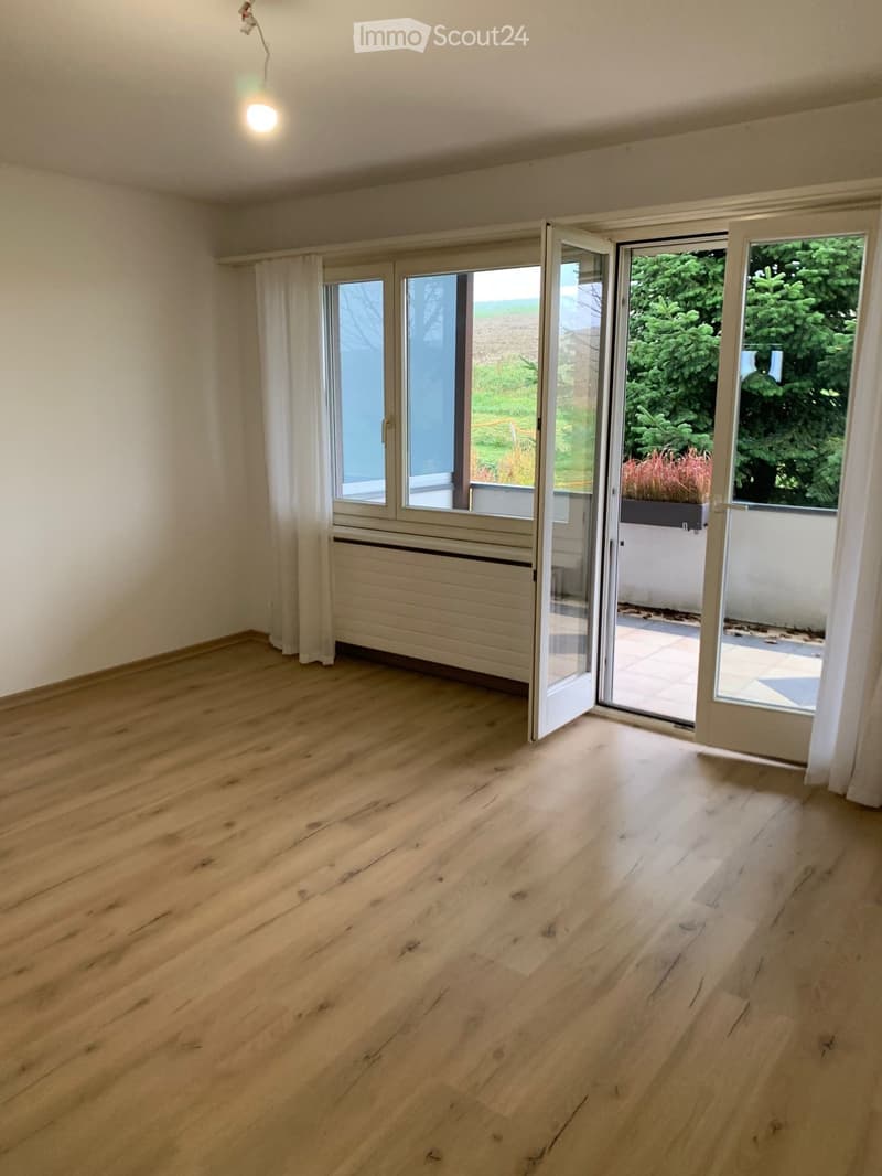Empty room with wooden flooring, large windows, and sliding glass doors leading to a balcony or outdoor area.