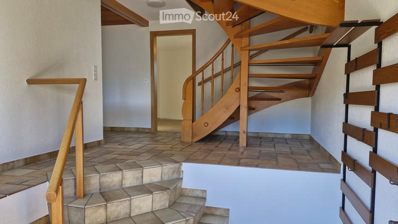 Hallway with a wooden staircase leading upwards, tiled floor, and white walls.