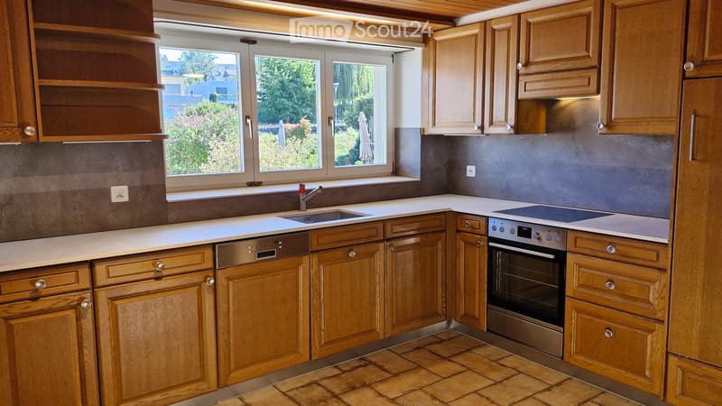 Modern kitchen with wooden cabinets, white countertops, stainless steel appliances, and a large window overlooking a garden.