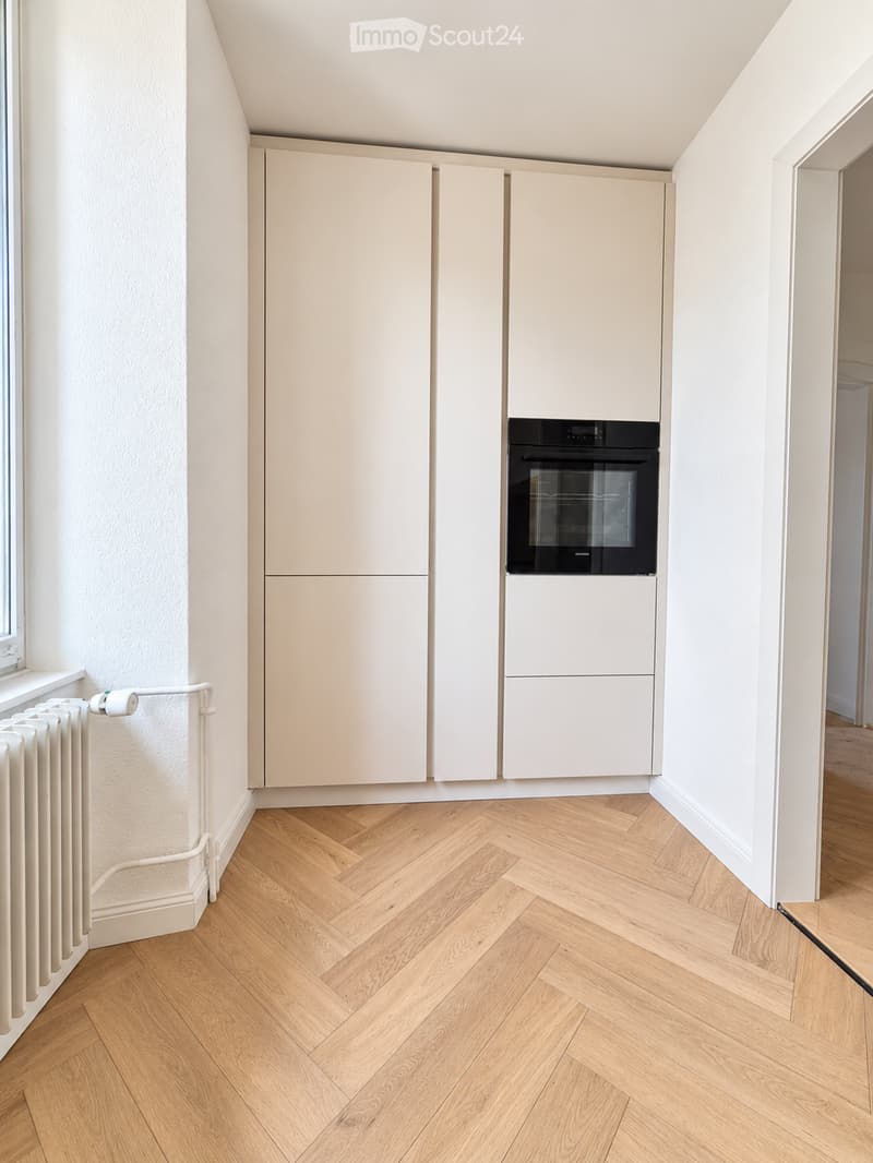 Modern kitchen with light-colored cabinets, a built-in oven, and herringbone wooden flooring.