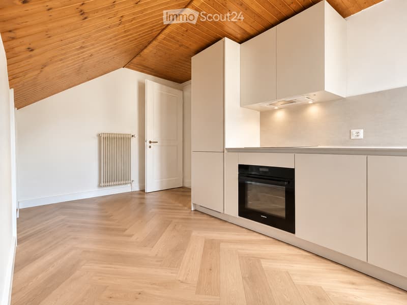 Modern kitchen with light-colored cabinets, wooden herringbone flooring, and a built-in oven. The ceiling has exposed wooden beams, and there is a radiator on the wall.