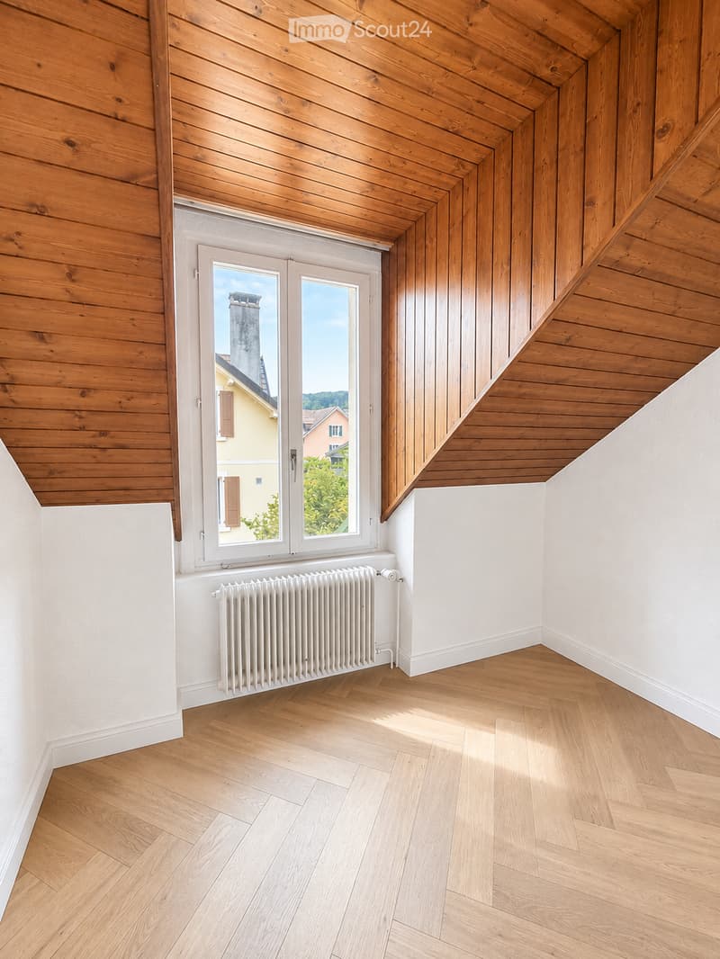 Empty room with wooden flooring, white walls, wooden ceiling, and a window with a radiator below it.