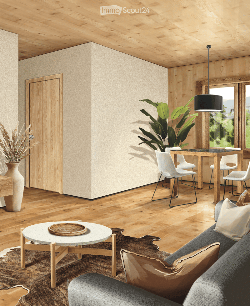 Modern living room with wooden floors, a grey sofa, coffee table, dining table with chairs, and a large potted plant near the window.