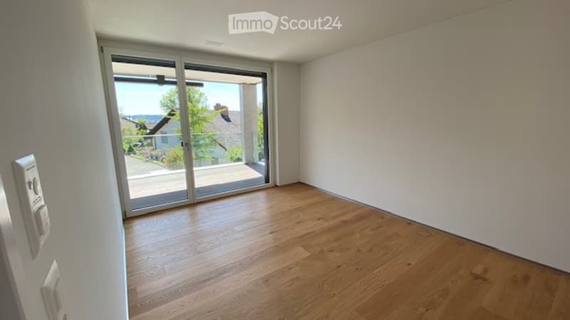 Empty room with wooden flooring, large sliding glass door leading to a balcony, white walls, and visible electrical outlets.