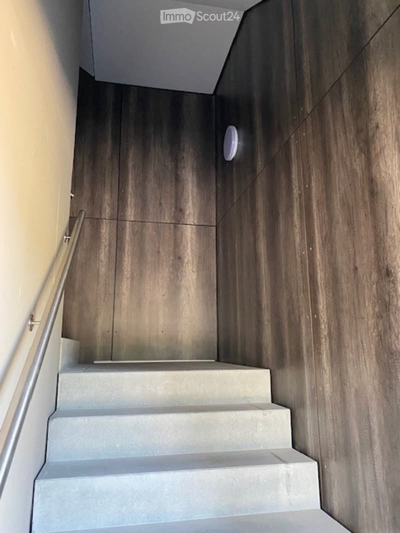 Modern staircase with wooden panel walls and a metal handrail, leading upwards.