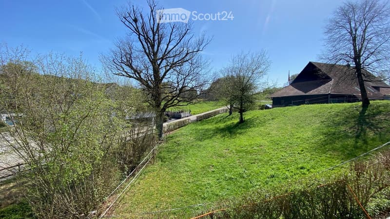 House on a hill, brown roof, surrounded by green grass and trees, clear blue sky