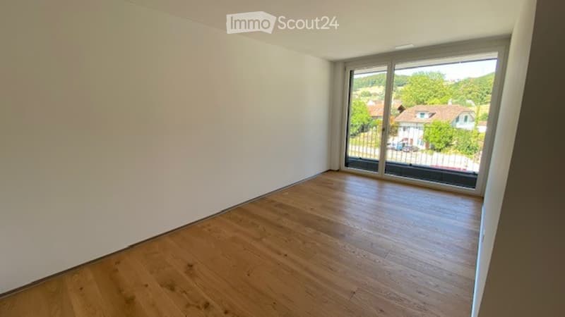 Empty room with wooden flooring and large window offering a view of the surrounding area.