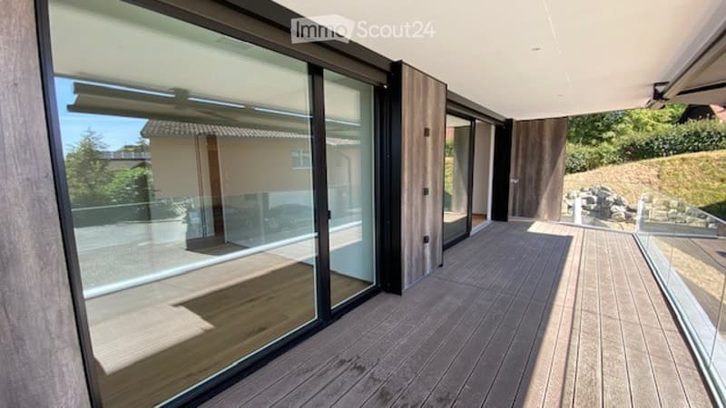 Modern balcony with wooden decking, large glass sliding doors, and a view of the surrounding greenery.