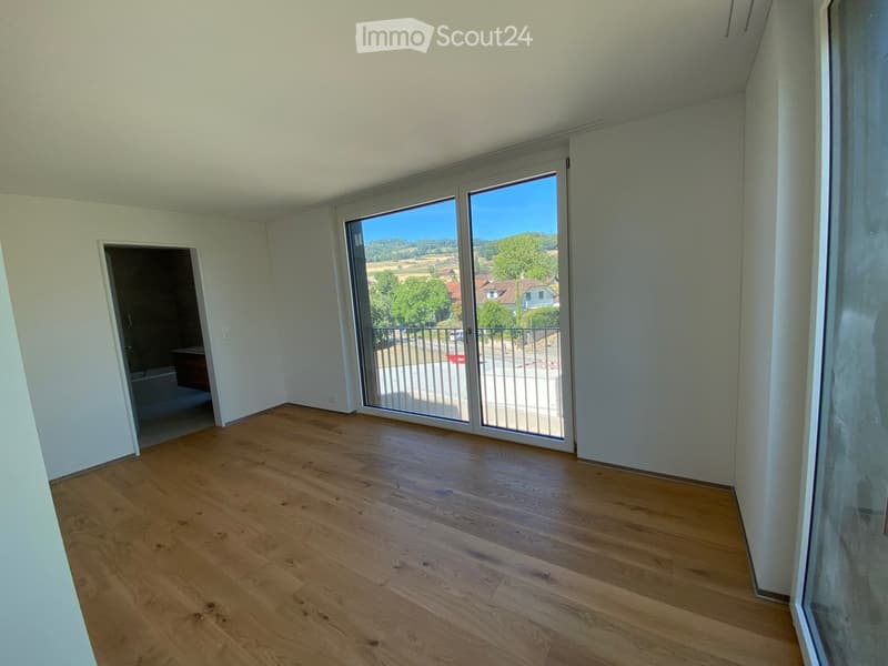 Empty room with wooden flooring, large sliding glass doors leading to a balcony, and a view of a green landscape.
