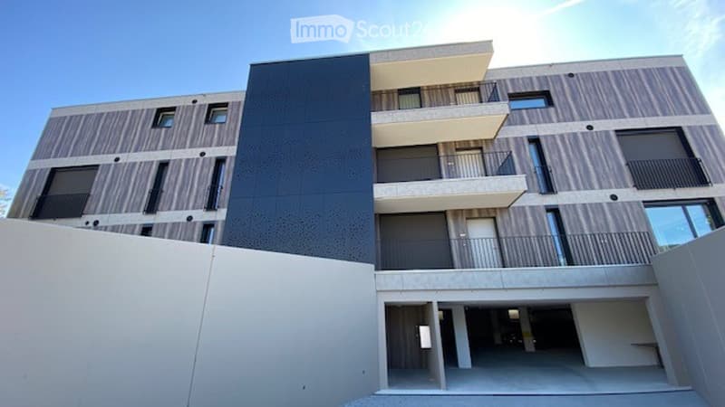 Modern multi-story apartment building with balconies, garage entrance, and contemporary facade design.