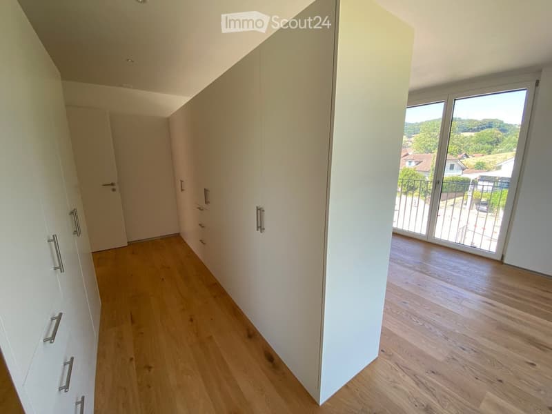 Empty hallway with light wooden flooring, white walls, built-in wardrobes, and a sliding glass door leading to a balcony with a scenic view.