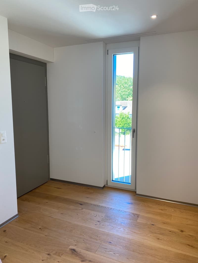 Empty room with wooden flooring, white walls, and a sliding glass door leading to a balcony.