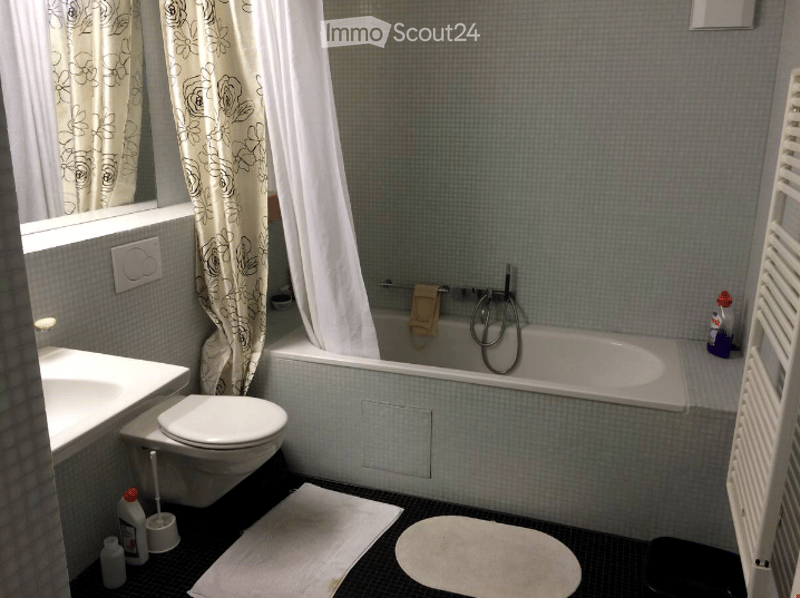 Bathroom with a bathtub, toilet, sink, and shower curtain. Cleaning supplies are placed near the sink and bathtub.