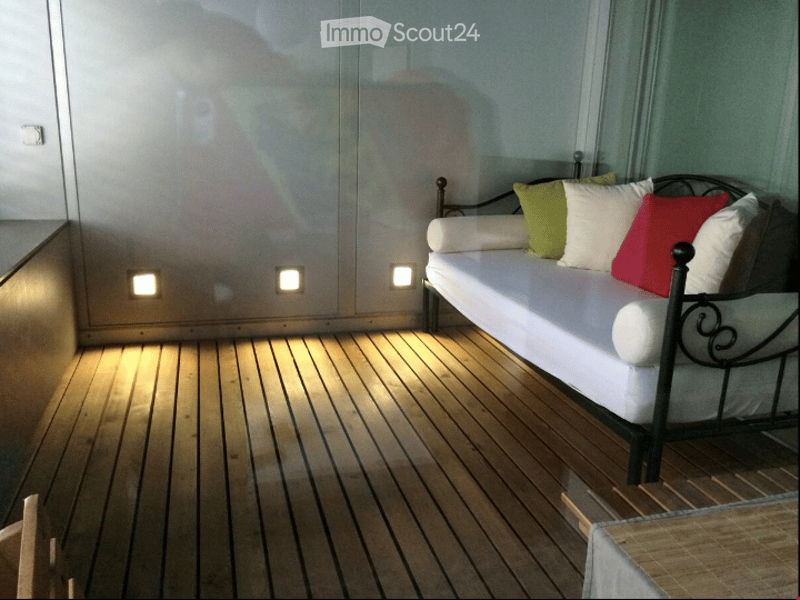 Cozy balcony with wooden decking, white sofa, and colorful pillows.
