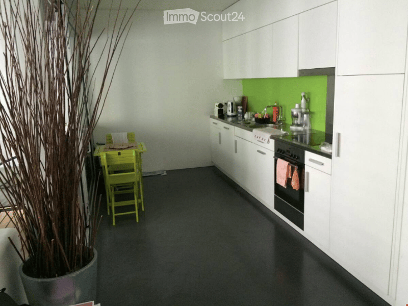 Modern kitchen with white cabinets, black countertops, and a green backsplash. Includes a small yellow table and chairs, a potted plant, and various kitchen appliances.