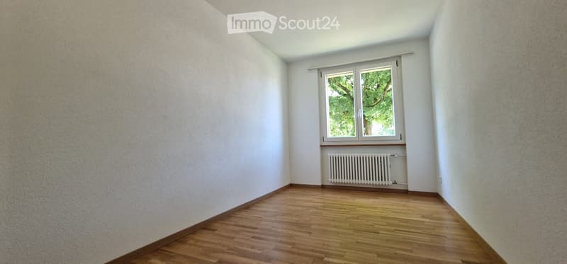 Empty room with wooden flooring, white walls, and a single window with a radiator below it.