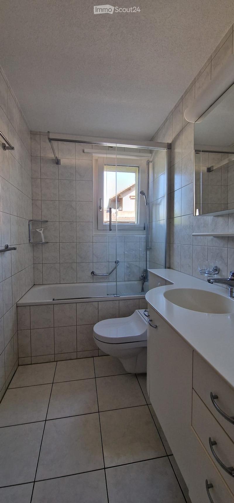 Modern bathroom with beige tiled walls and floor, featuring a bathtub, toilet, sink, and shower area with a glass enclosure.