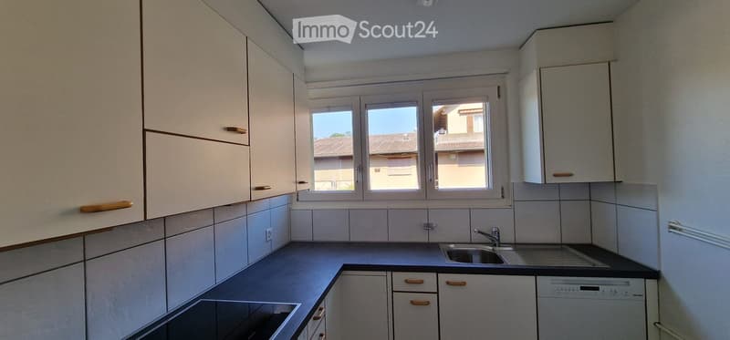 Modern kitchen with white cabinets, tiled backsplash, and a window overlooking a residential area.