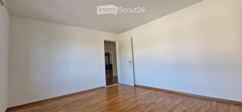 Empty room with light-colored walls and wooden flooring, featuring two open doors leading to adjacent spaces.