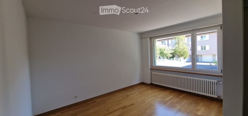 Empty room with wooden flooring, white walls, and a large window with a radiator below it.
