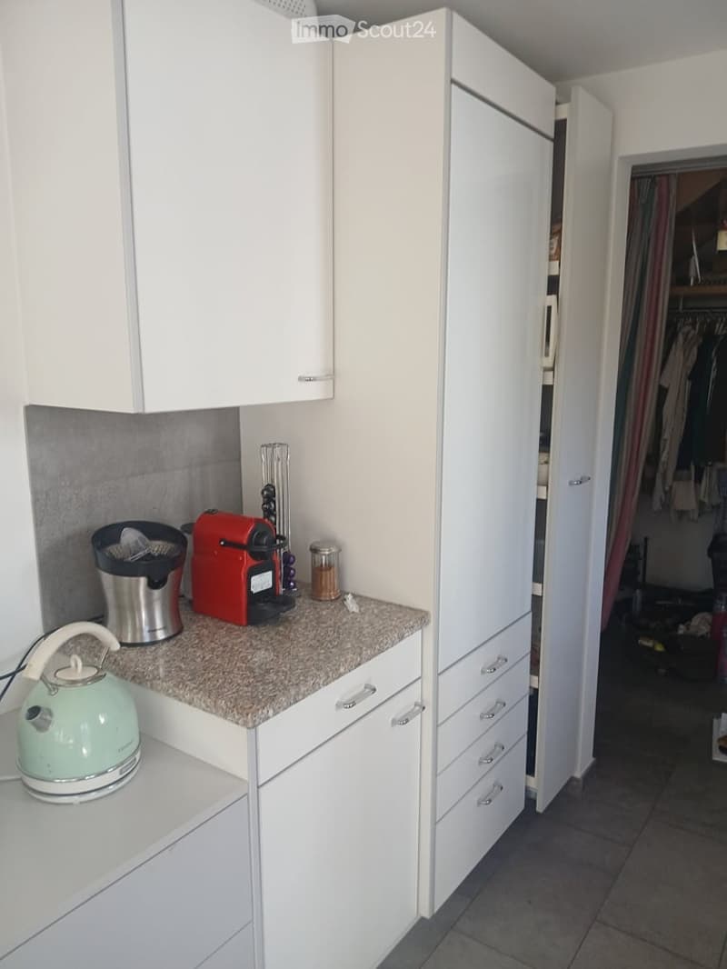 Modern kitchen with white cabinets, granite countertop, and various appliances including a coffee maker, kettle, and blender.