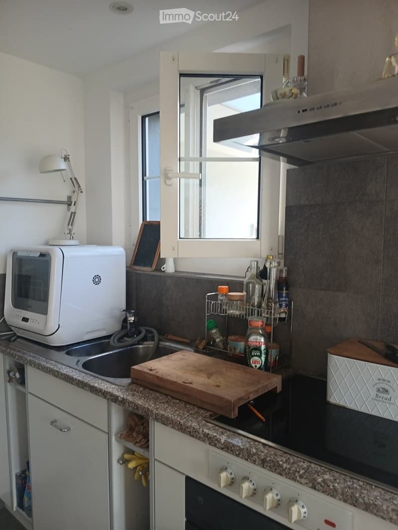 Modern kitchen with granite countertops, white cabinets, microwave, sink, cutting board, and various kitchen items on the counter.