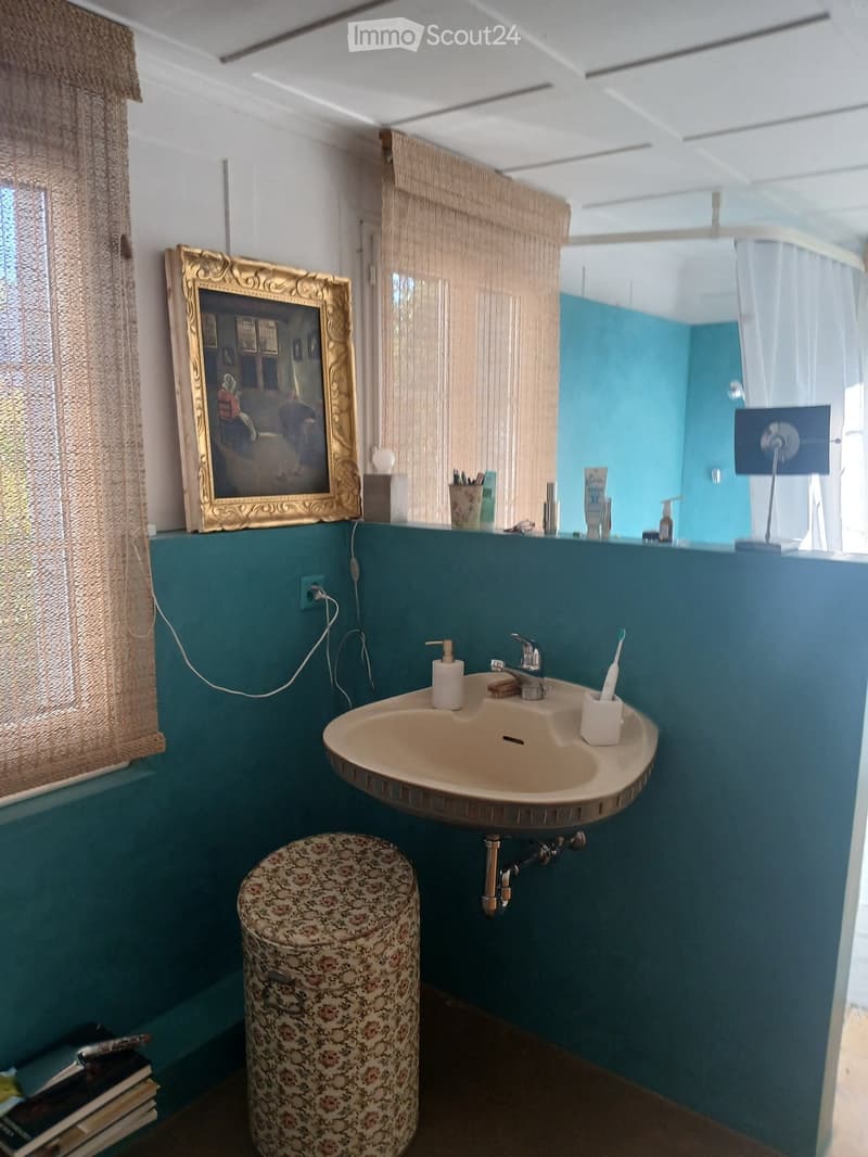 Bathroom with teal walls, a sink with a modern faucet, a floral-patterned stool, a mirror, and a framed picture on the wall.