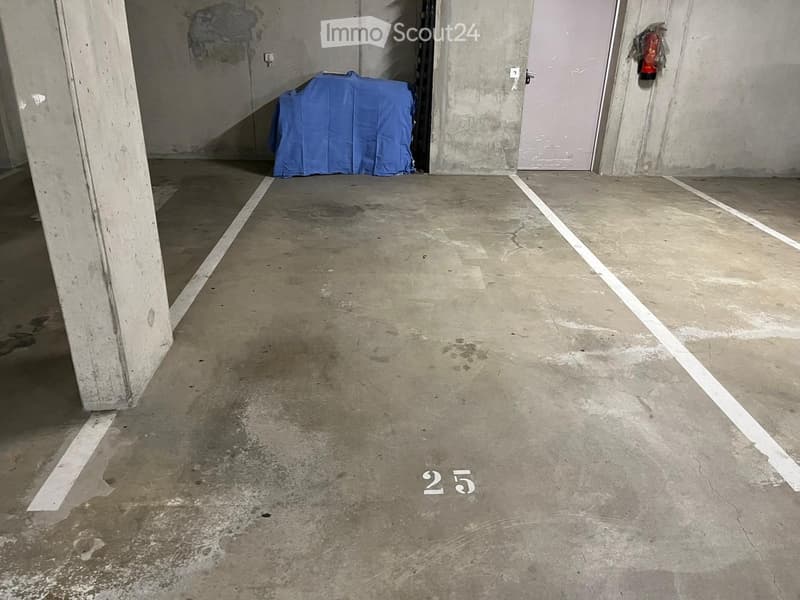 Empty room with concrete floor, white lines marking dimensions, and a blue-covered object in the background.