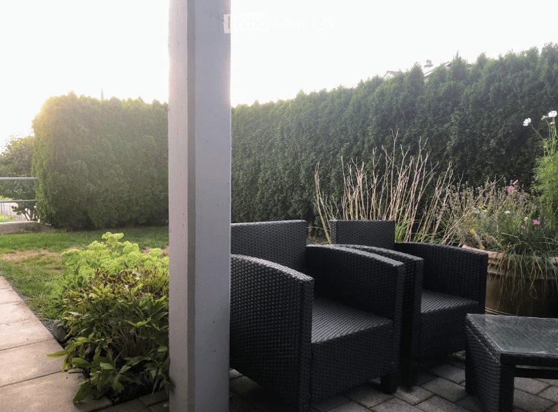 A well-maintained garden area with neatly trimmed hedges, a variety of plants, and a small seating area featuring wicker chairs and a glass-top table.