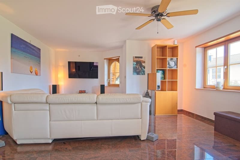 Modern living room with white leather sofa, wooden shelf, table lamp, floor lamp, television, and a ceiling fan.