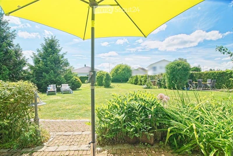 A well-maintained garden with a large umbrella, lounge chairs, a dining set, and lush greenery.