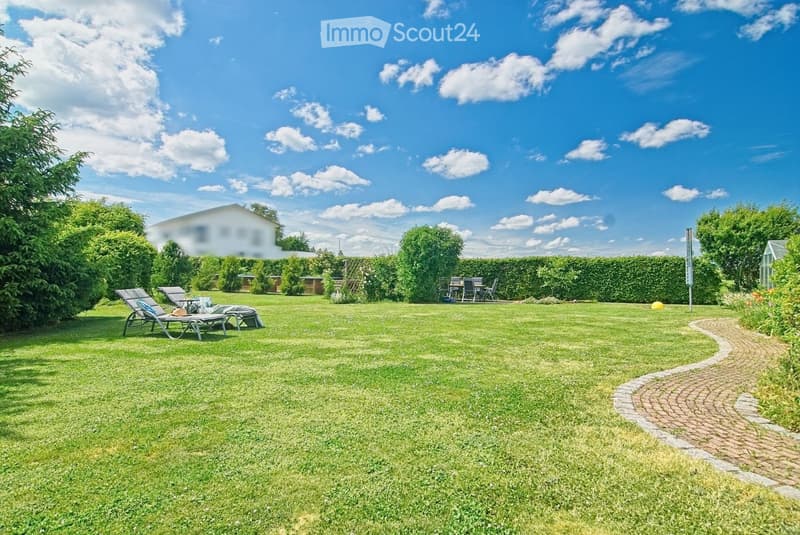 Well-maintained garden with a large lawn, lounge chairs, a dining set, and a curved brick pathway.