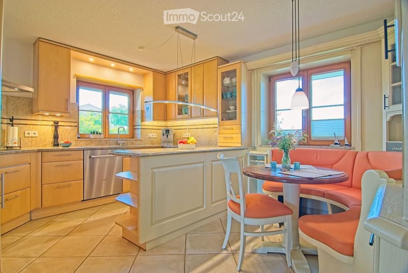 Bright kitchen with light wood cabinetry, a central island, and a round dining table with seating. Stainless steel appliances, pendant lights, and large windows provide natural light.