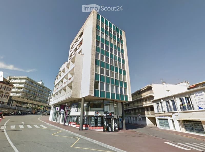 A modern multi-story building with a mix of glass and concrete facade, located on a street corner with adjacent buildings and signage.