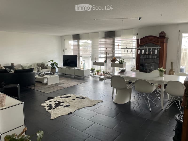 Modern living room with dark tiled flooring, a white dining table with chairs, a black sofa, a coffee table, a television, and decorative items including vases and plants.